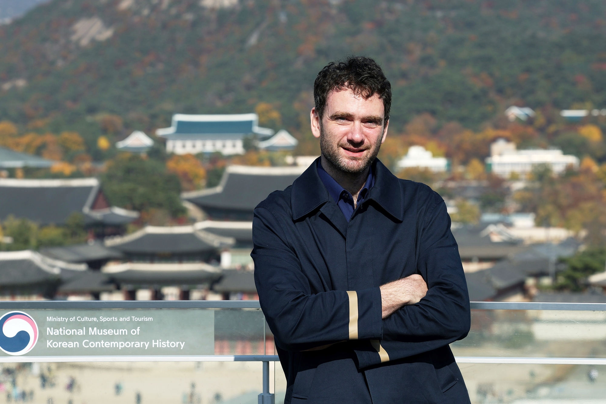 Daniel Tudor, a Seoul-based British author who has written several nonfiction books on Korea, on Nov. 13 poses for a photo on the roof of the National Museum of Korean Contemporary History in Seoul, with Gyeongbogkung Palace shown in the background. (Lee Jun